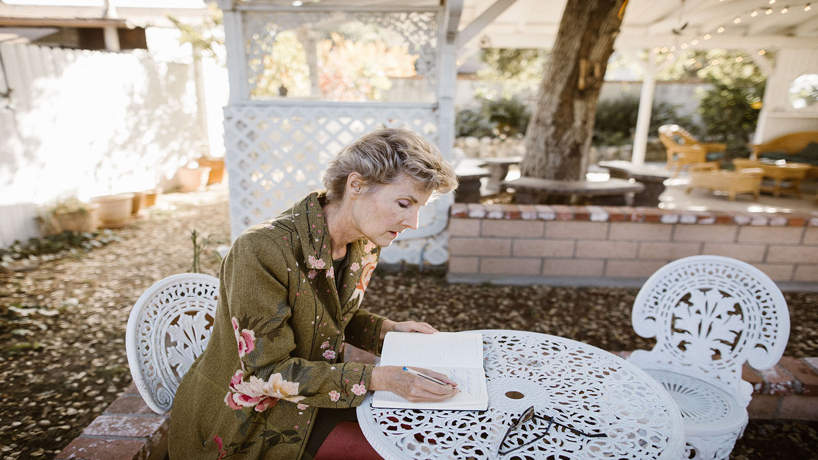 Older woman writing thoughtfully in a notebook at a garden table