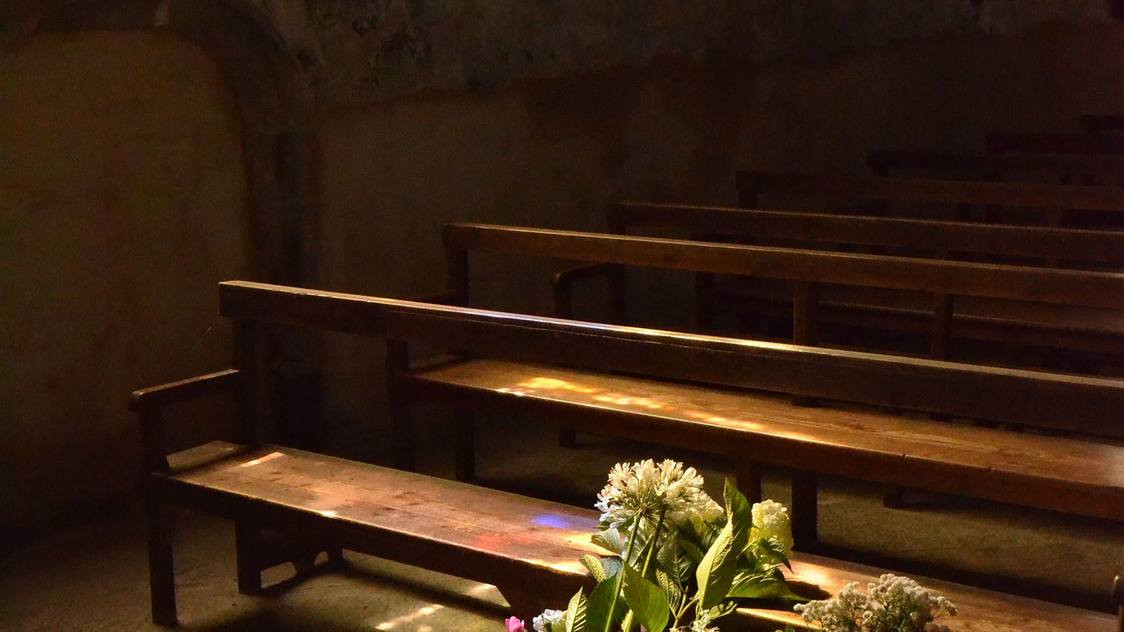 Empty wooden pews and floral arrangements inside a quiet chapel