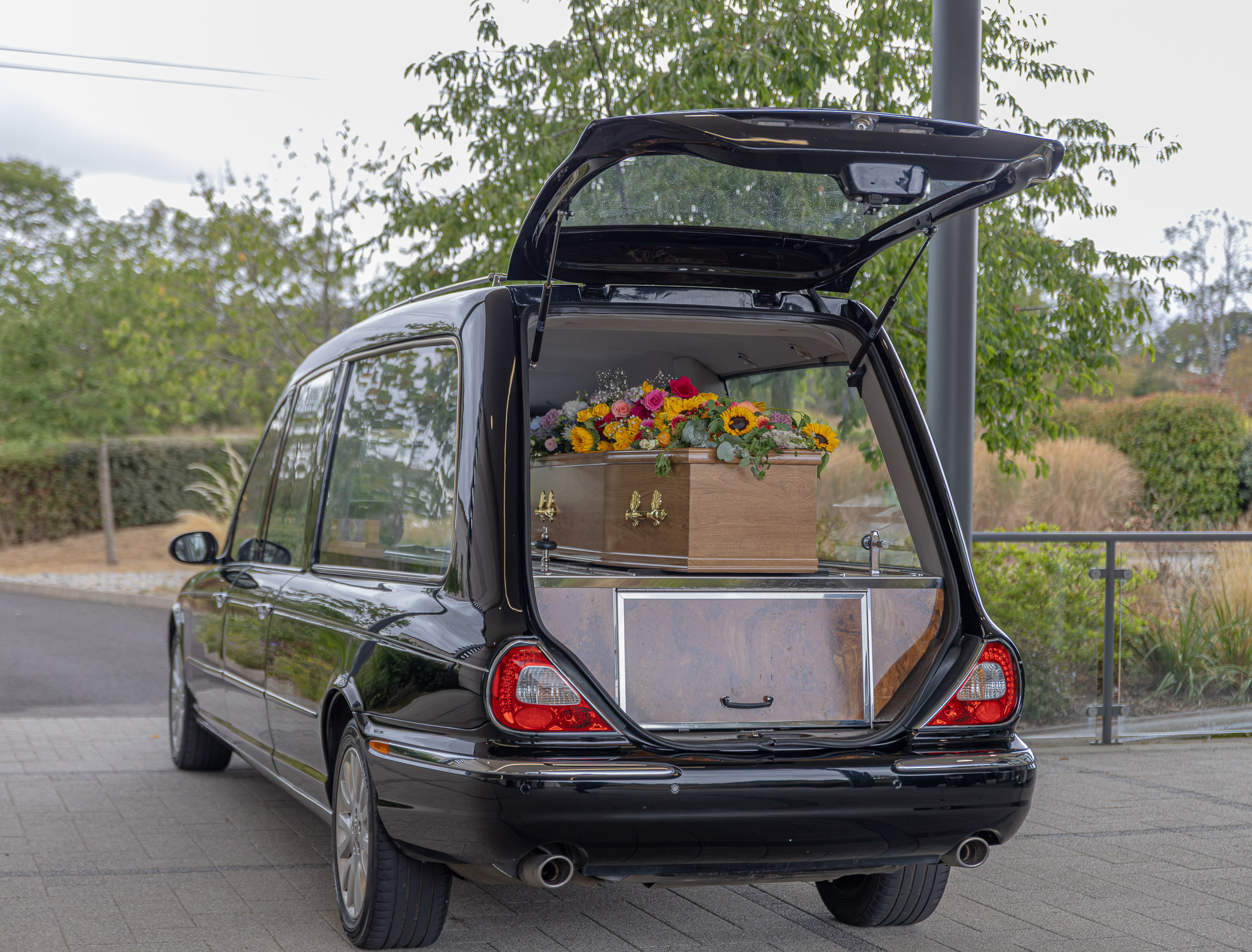 The Wealden hearse carrying a wooden coffin and colourful floral tribute at the crematorium