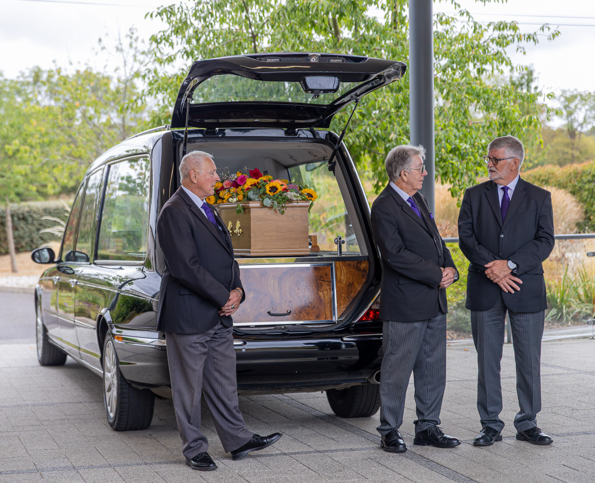 The Wealden hearse at the crematorium with a wooden coffin and floral tribute